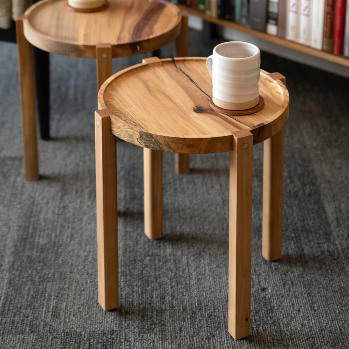 Two wooden side tables with white mugs in a room with books on shelves.