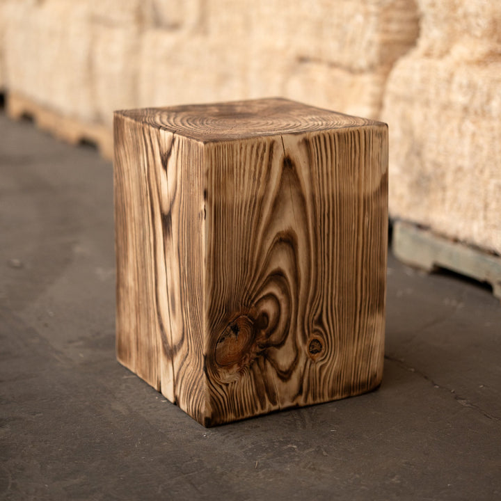 Wooden cube on a dark surface with stacked bales of hay in the background