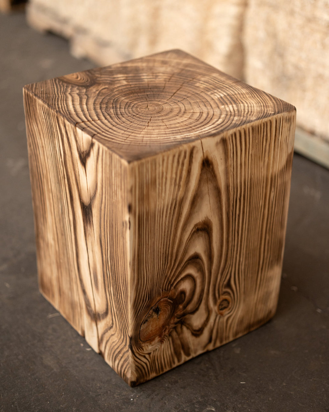 Wooden cube stool on a dark floor with a blurred beige background