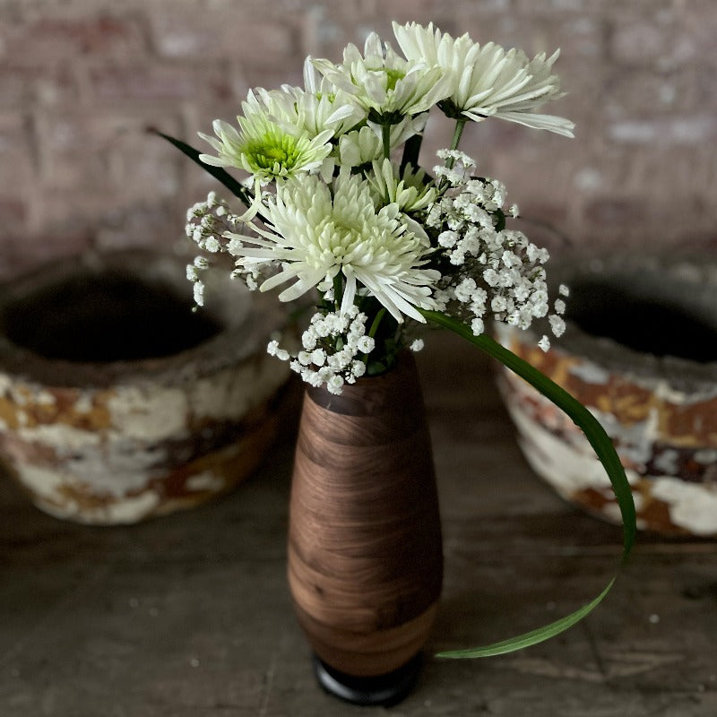 Wooden vase with flowers pictured against brick