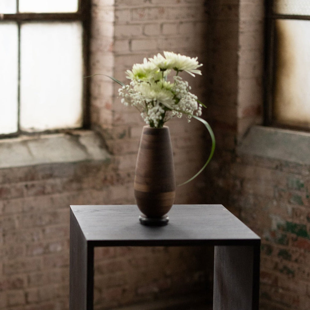 Wooden vase with flowers and a bronze base against antique bricks
