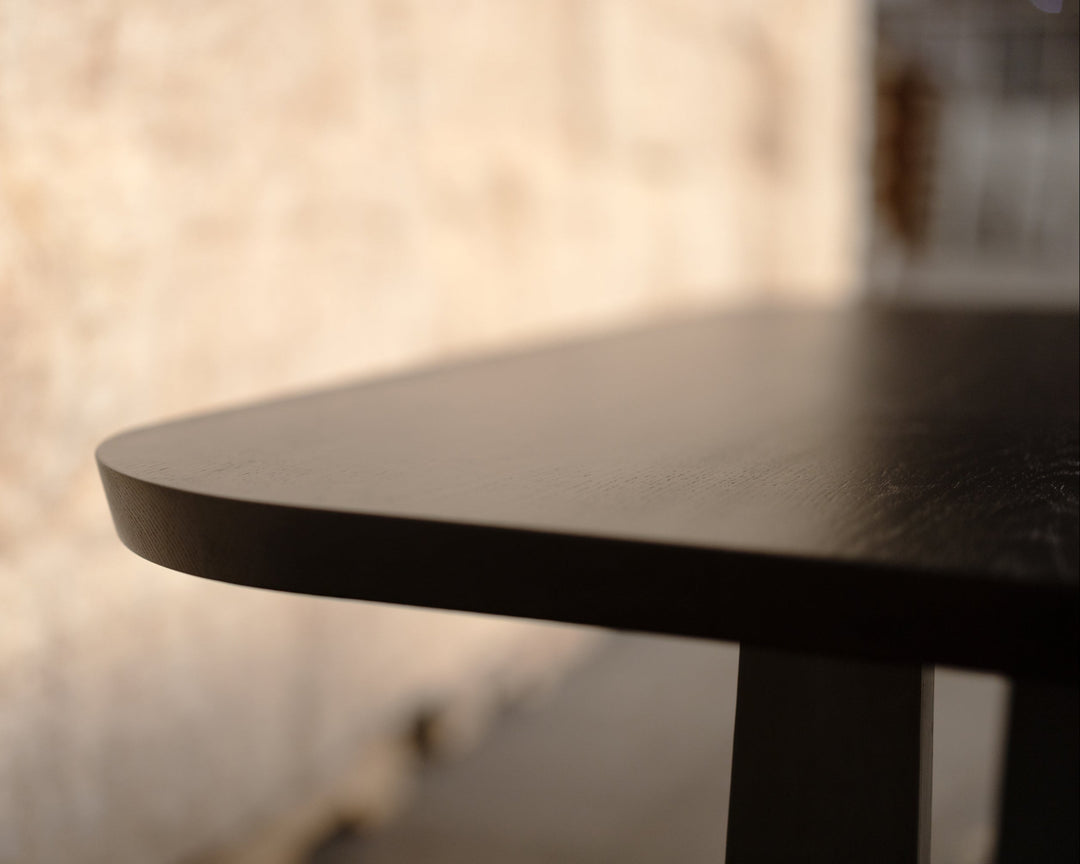 Close-up of a dark wooden table with a  curved corner and blurred background