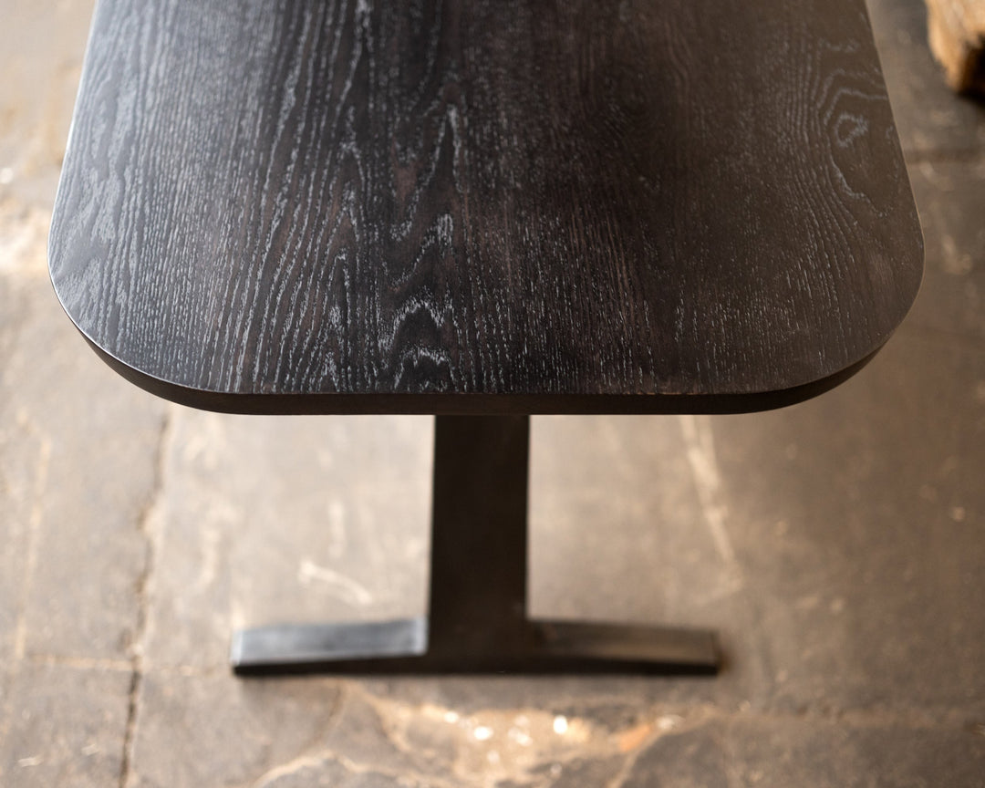 Dark wooden table with a modern metal pedestal base on a stone floor