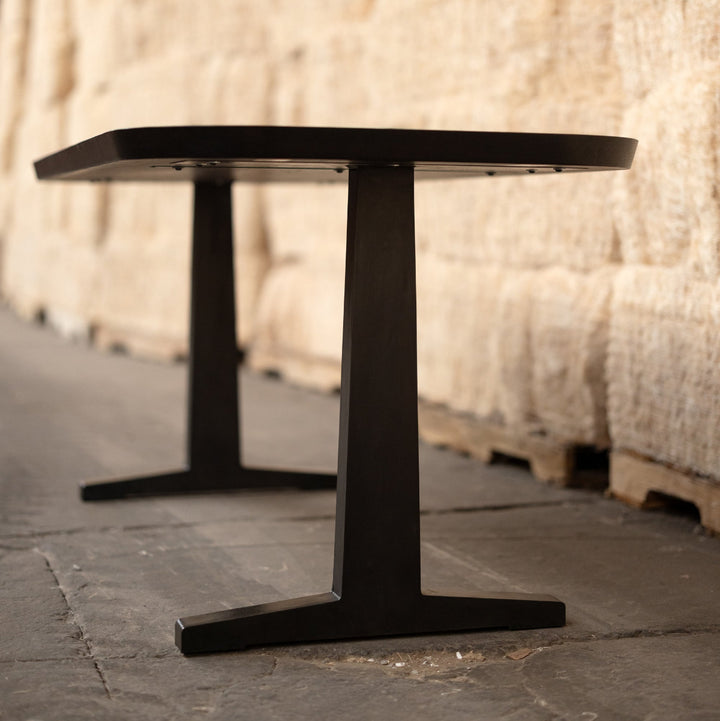 Black metal and wood table in a warehouse setting with stacked bales of hay.