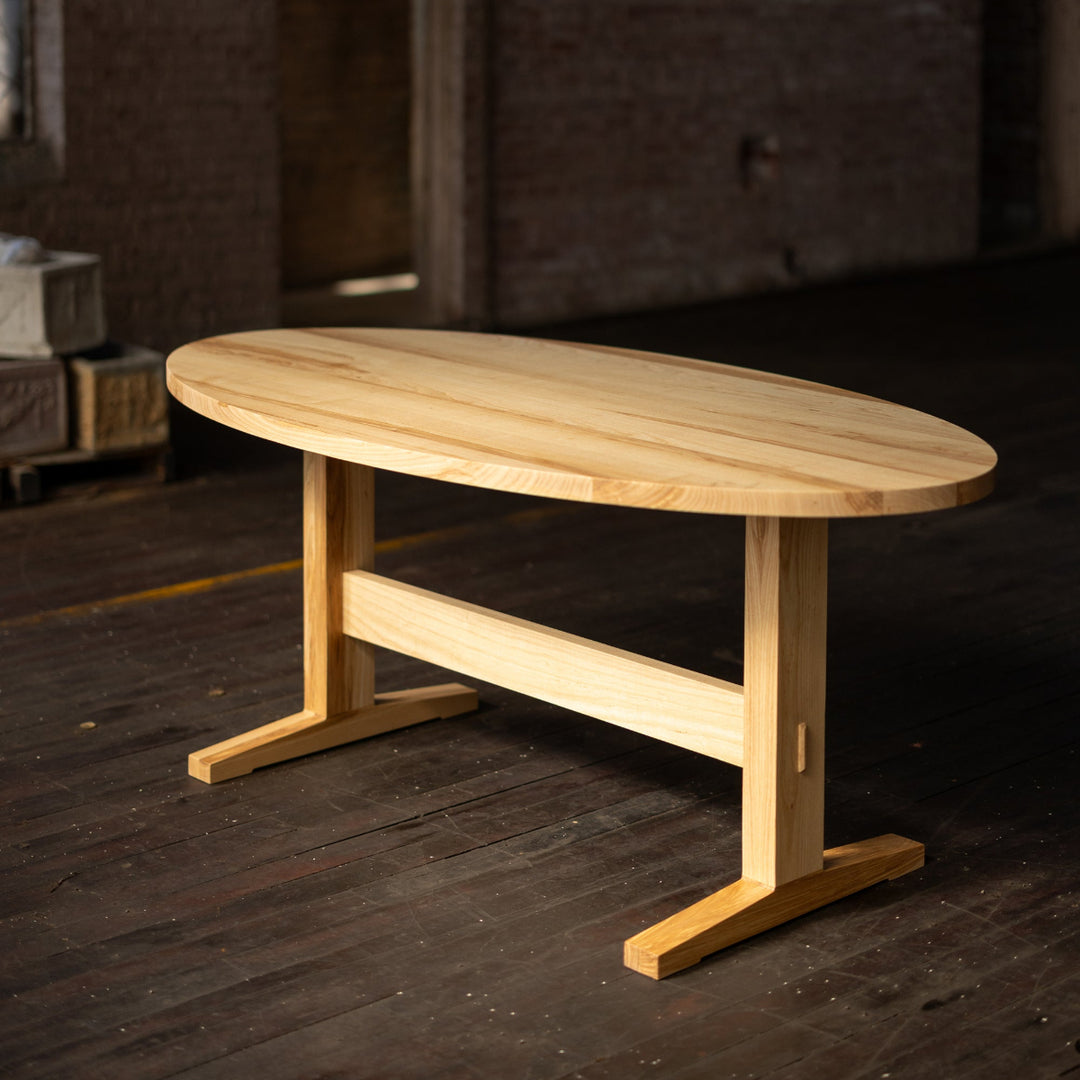 Ash Wooden table on a pedestal base in a dimly lit room with brick walls