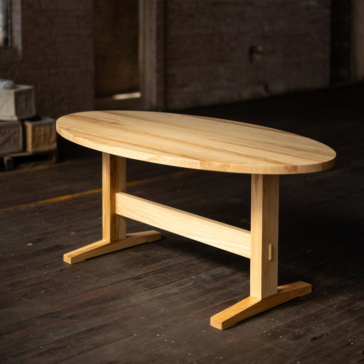 Ash Wooden table on a pedestal base in a dimly lit room with brick walls